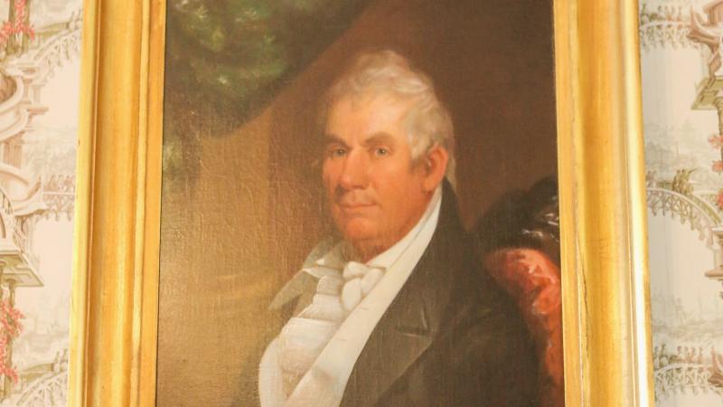 Portrait of a man in a gold frame on patterned wallpaper.