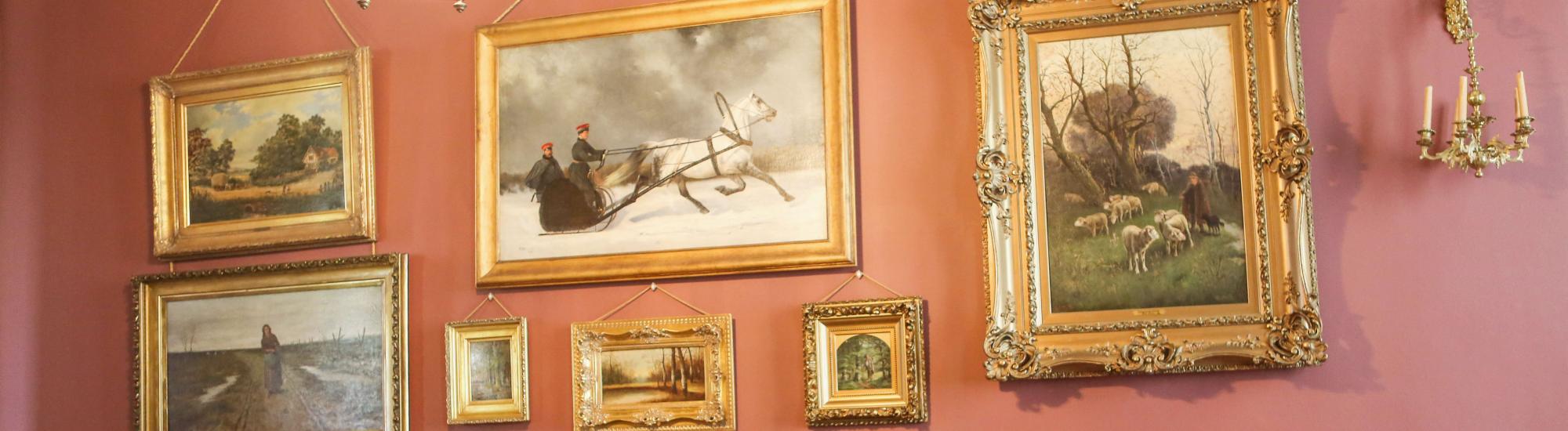 Elegant room with vintage paintings, a black sofa, two red chairs, and soft lighting.