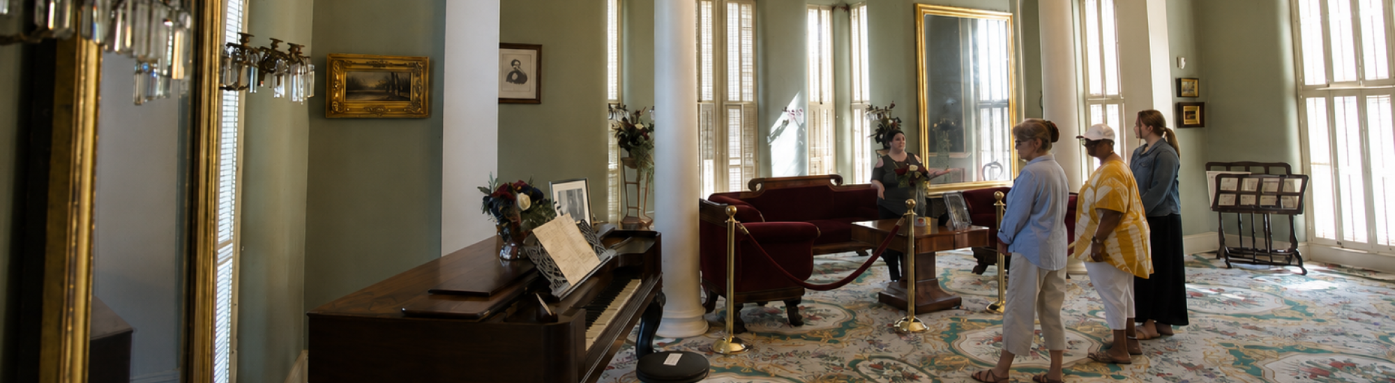 Lavish room with chandelier, piano, and visitors examining furniture.