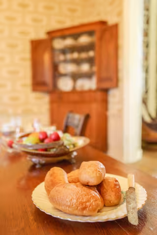 Bread and butter on a plate on a wooden table, with a fruit bowl and china cabinet in the background.