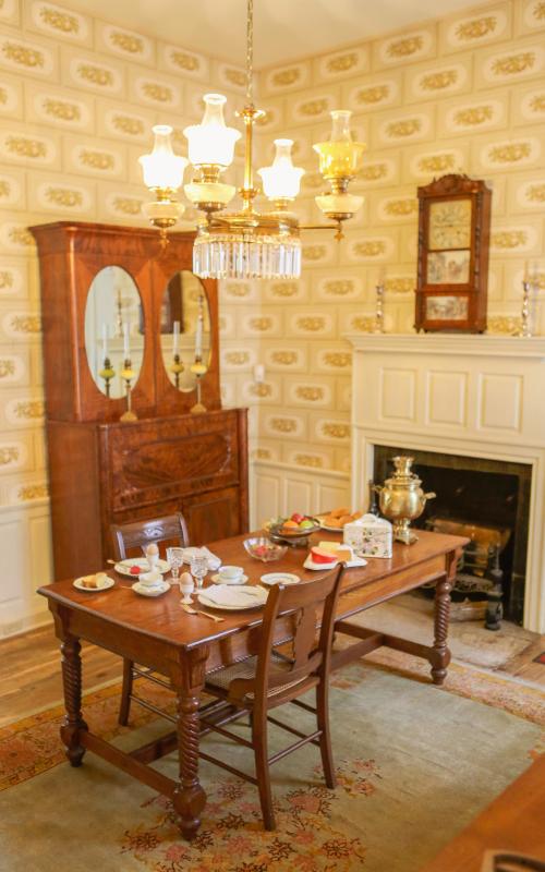 Vintage dining room with wooden table, chairs, china cabinet, and ornate chandelier.