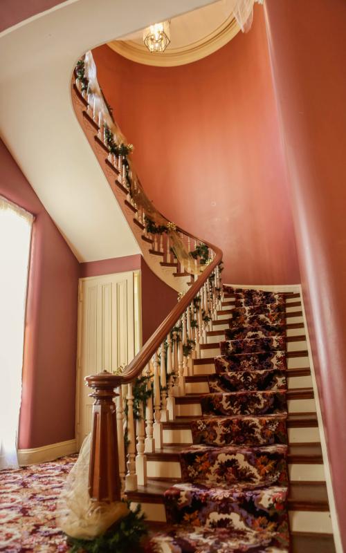 Curved staircase with floral carpet and garland, red walls.